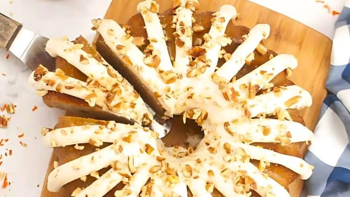 Round cake with white icing and chopped nuts on top, sliced and served on a wooden board.