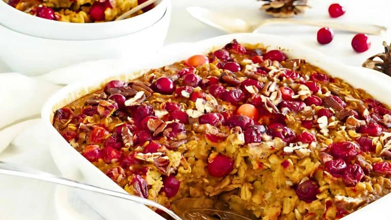 A dish of baked oatmeal topped with fresh cranberries and chopped pecans, with a serving spoon on the side.