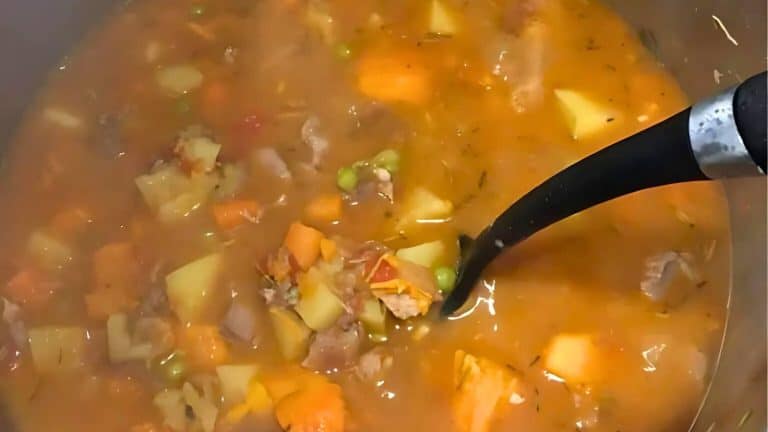 A pot of hearty stew with chunks of vegetables, meat, and peas in a thick broth, being stirred with a black ladle.