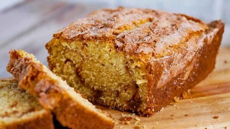 A loaf of cinnamon bread with a sugar topping is sliced on a wooden cutting board.