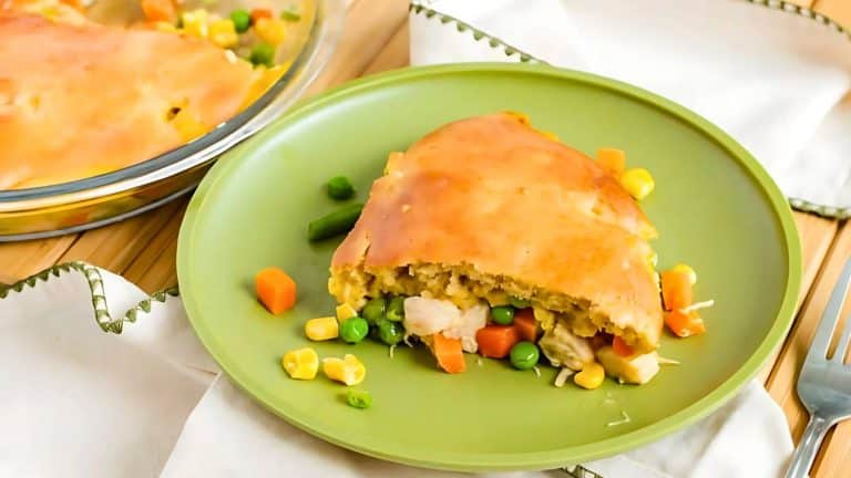 Slice of pot pie with vegetables on a green plate, set on a wooden table with a white napkin nearby.