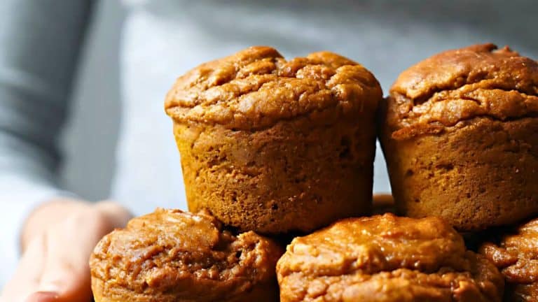 A stack of golden-brown muffins held in a person's hands, with a focus on their textured tops.