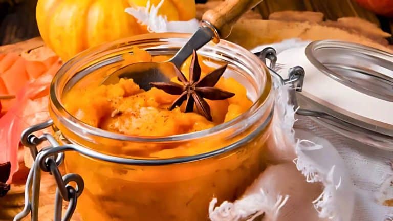 A jar of pumpkin puree with a star anise garnish next to a lid, surrounded by cloth and pumpkins.