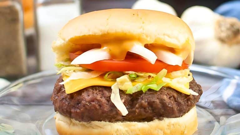 A cheeseburger with lettuce, tomato, onions, and a slice of cheese on a bun.