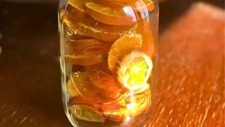 A glass jar filled with transparent liquid and sliced lemons is placed on a wooden surface.