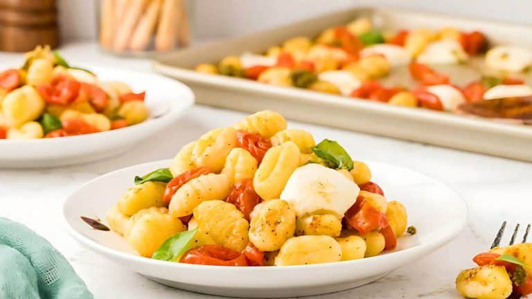 A plate of gnocchi with tomatoes, mozzarella, and basil. Another dish and a baking tray with the same ingredients are in the background.