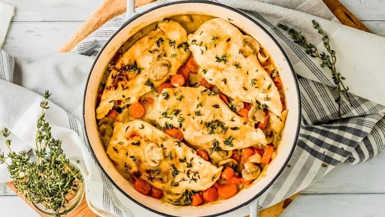 A pot containing cooked chicken breasts with mushrooms, carrots, and herbs. Plates and a napkin are nearby.