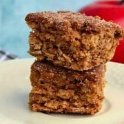 Two stacked oatmeal cake squares on a plate, with a red apple in the background.