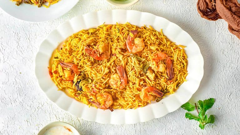 A white oval dish with yellow rice mixed with shrimp and vegetables, garnished with herbs.