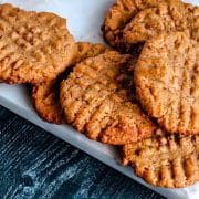 Freshly baked peanut butter cookies arranged on white parchment paper on a dark wooden surface.