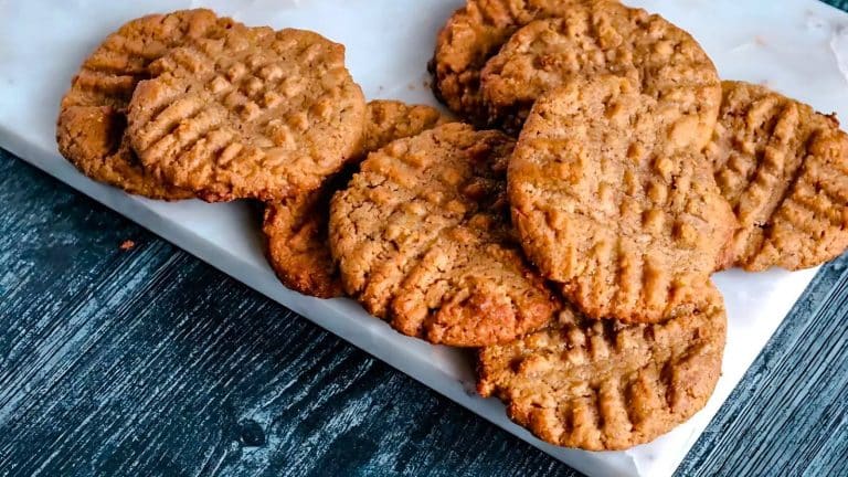 Freshly baked peanut butter cookies arranged on white parchment paper on a dark wooden surface.