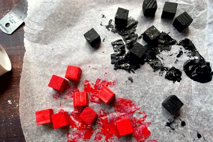 Red and black painted wooden cubes drying on parchment paper.