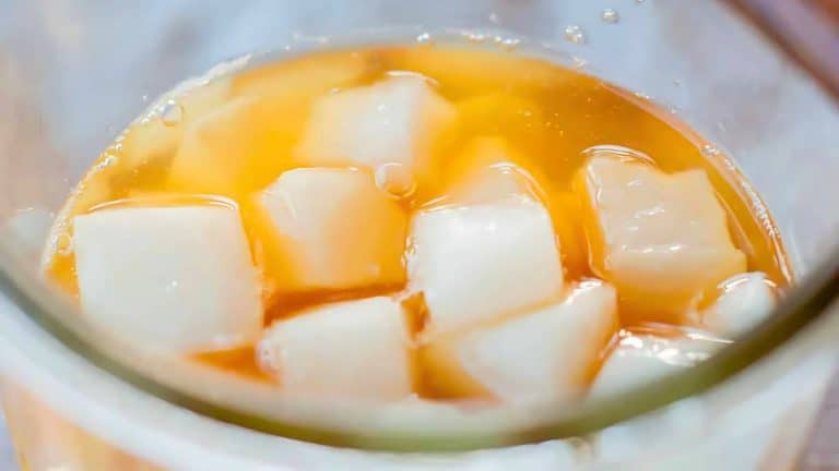 Close-up of a glass containing orange liquid with white ice cubes floating on top.
