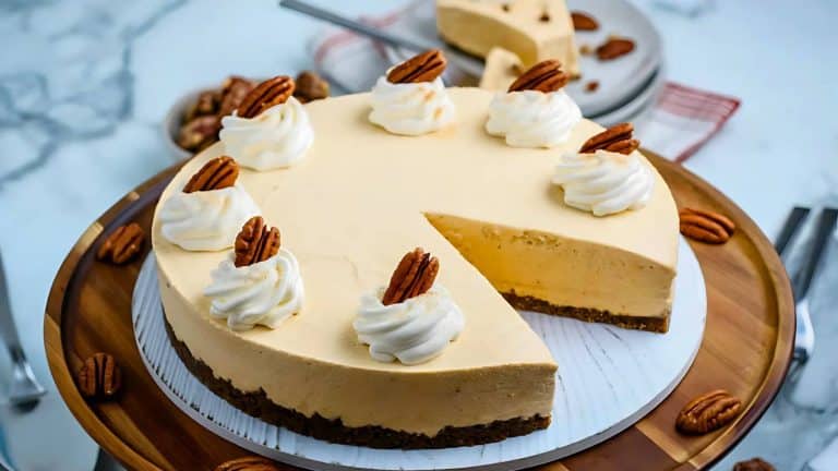 A round cheesecake topped with whipped cream and pecans, with a slice missing, on a wooden platter.