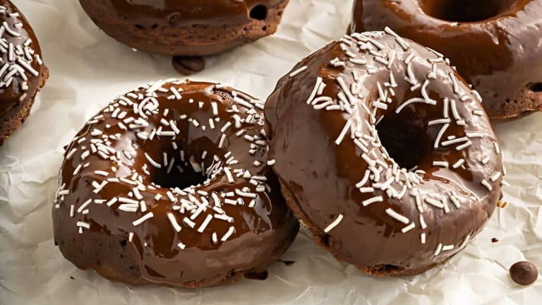Two chocolate-glazed donuts with white sprinkles on parchment paper.