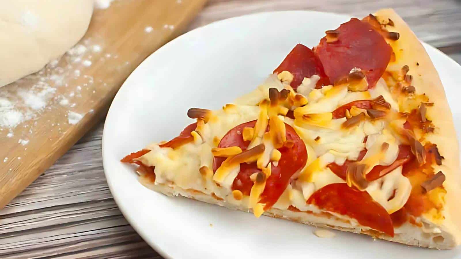 A slice of pepperoni pizza with melted cheese on a white plate, next to a wooden board with dough.