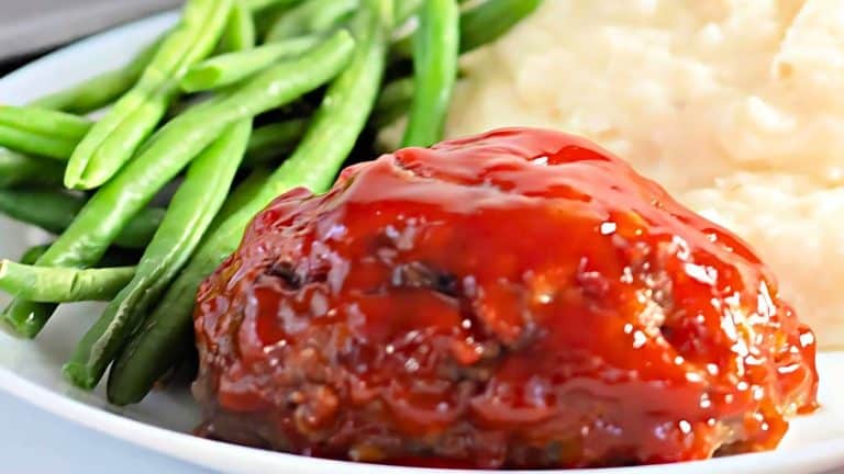 Plate with meatloaf covered in red sauce, green beans, and mashed potatoes.