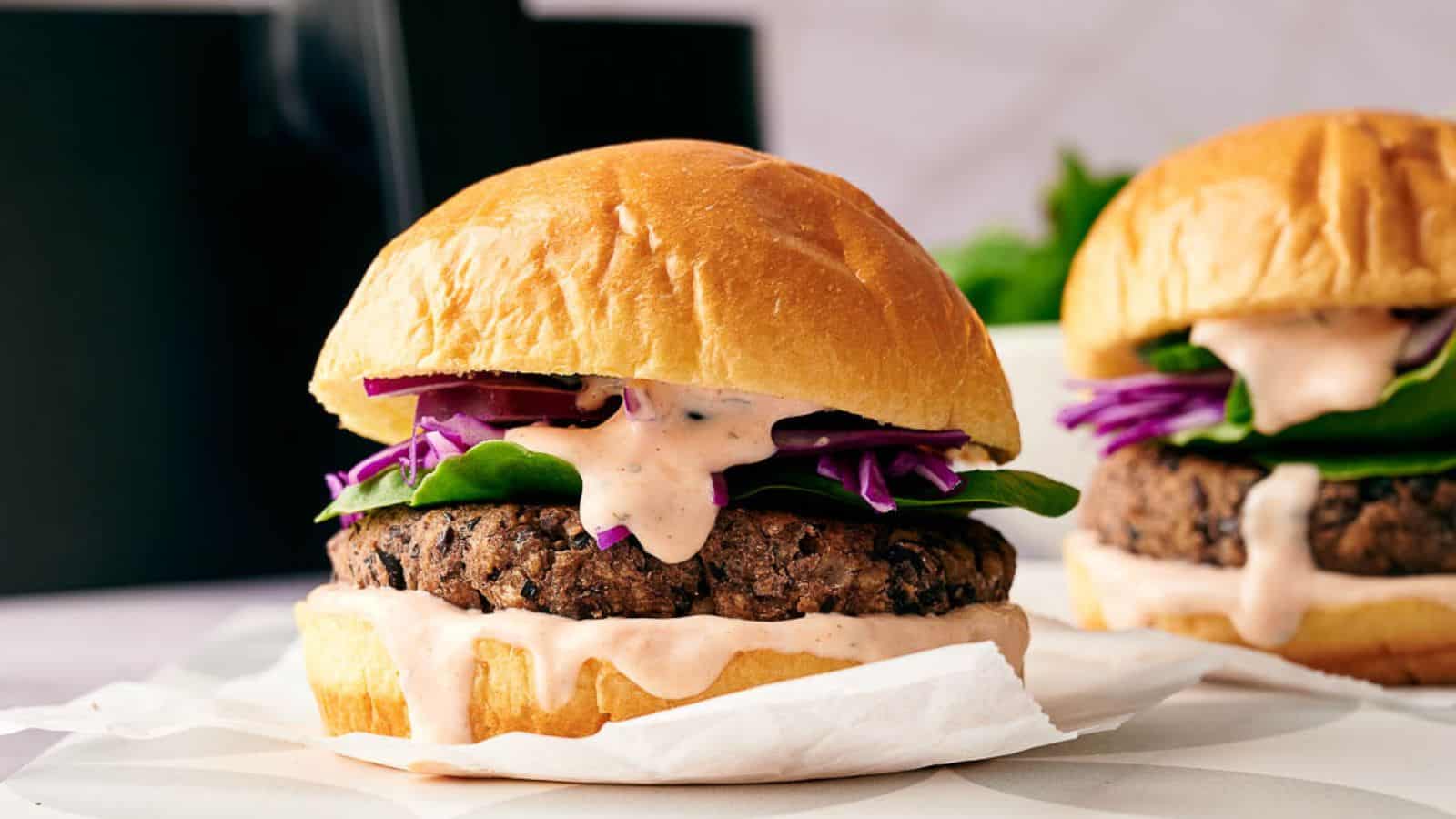 Close-up of a veggie burger with spinach, red cabbage, and sauce on a bun, wrapped partially in paper.