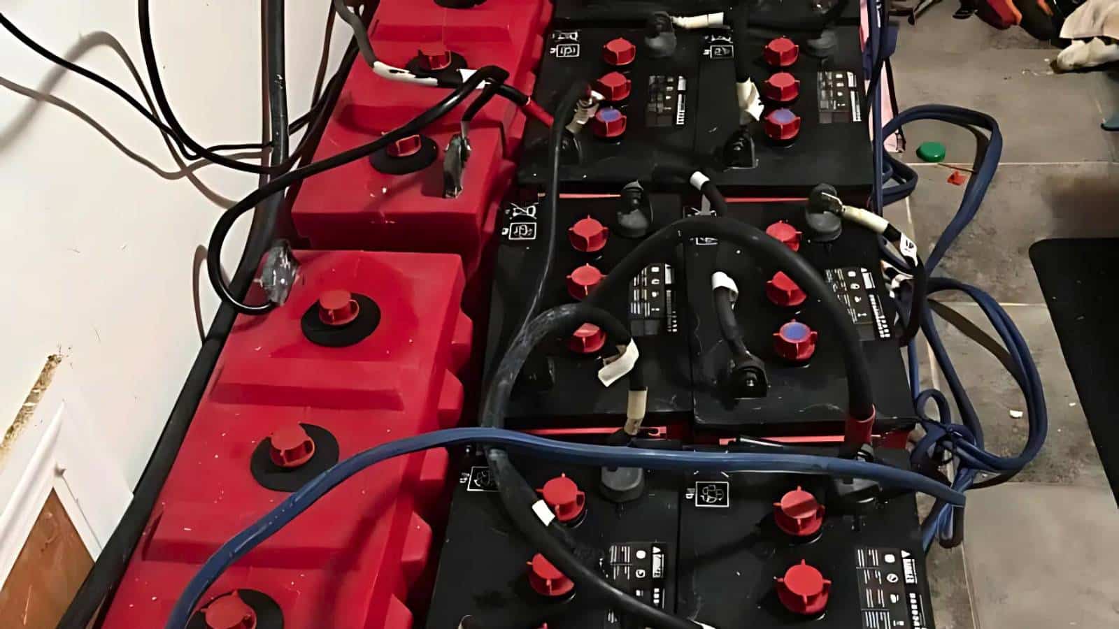 A row of wired red and black batteries lined up on a concrete floor with cables connecting them.