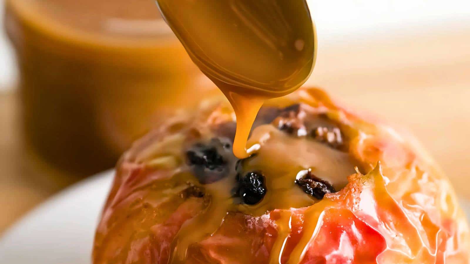 Caramel sauce being poured over a baked apple with raisins.
