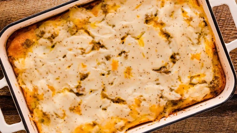 A baked casserole dish filled with layered cheesy mashed potatoes, topped with specks of herbs and spices.