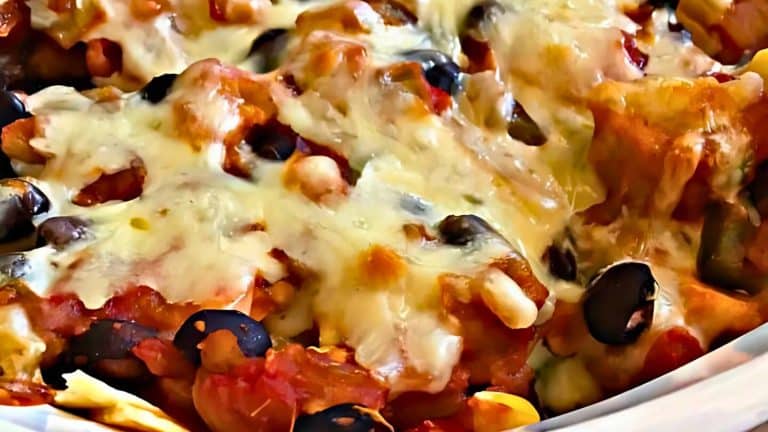 A close-up of baked nachos topped with melted cheese, black olives, and tomatoes.