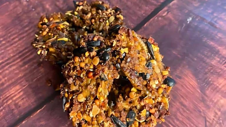 A close-up of three nut-seed clusters on a wooden surface, showcasing a mixture of various nuts and seeds bound together.