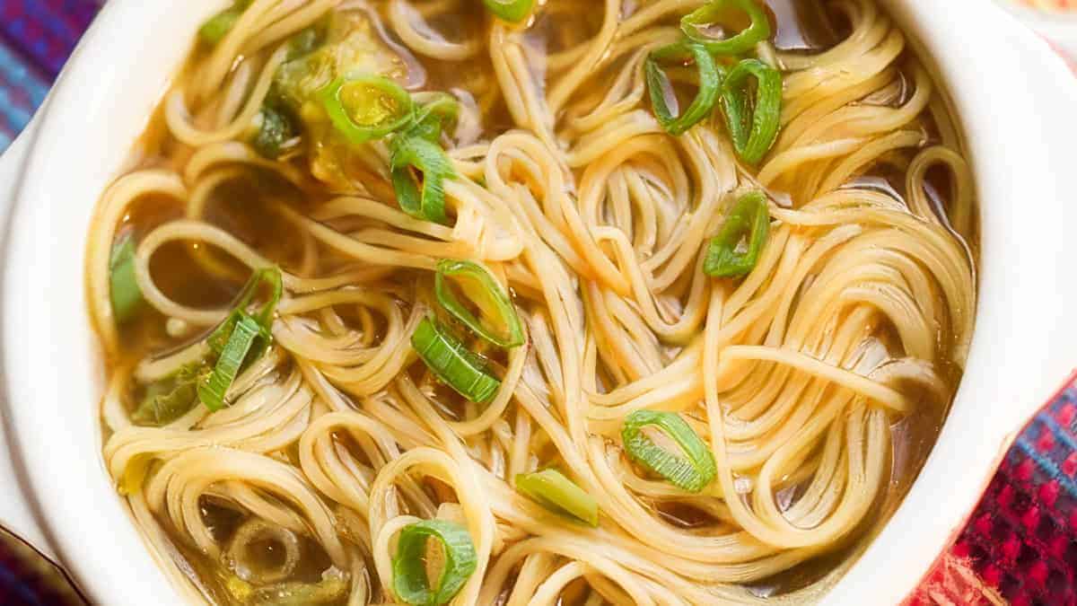 A bowl of noodle soup with sliced green onions on top.