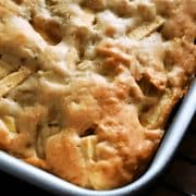 A close-up of a freshly baked apple cake in a rectangular baking dish, sitting on a cooling rack.