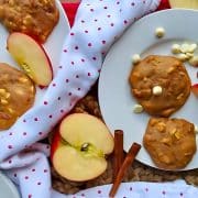 Plates with cookies, apple slices, and white chocolate chips on a polka dot napkin, surrounded by apple slices and cinnamon sticks.