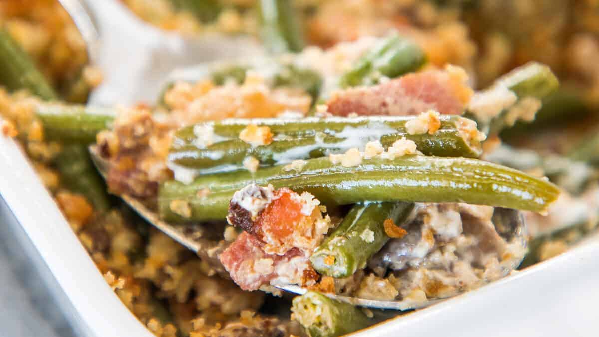 Close-up of a green bean casserole with crispy topping and bacon pieces, served on a spoon.