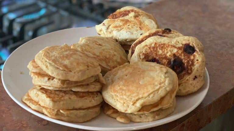 A plate of homemade pancakes, some plain and some with berries, stacked on a countertop.