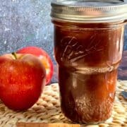 A mason jar with apple butter, apples and a knife next to it.