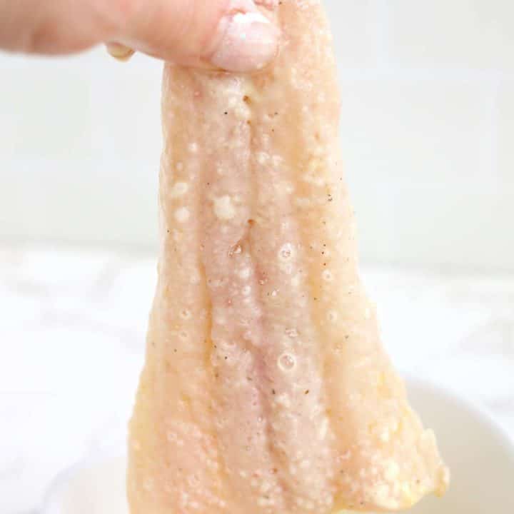 A person holding a piece of white fish in a bowl.