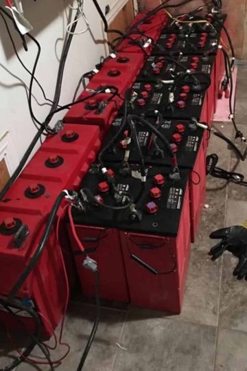 a picture of a few dozen red surrette batteries connected by cables in series.