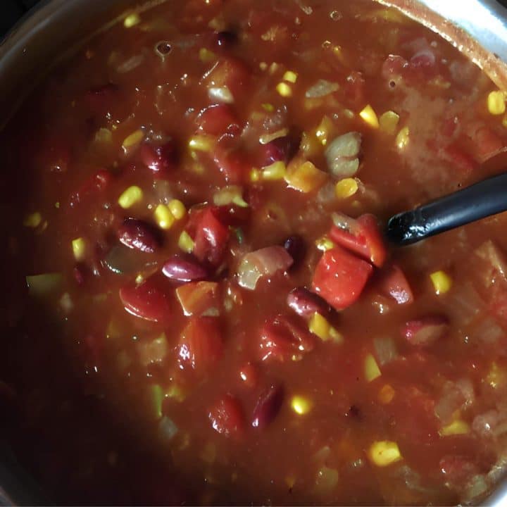 A pot of soup with corn, beans and tomatoes.