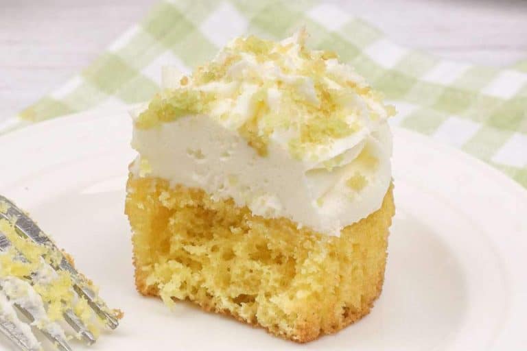 A slice of coconut cake with lime frosting and lime zest on top, displayed on a plate with a fork on the side.