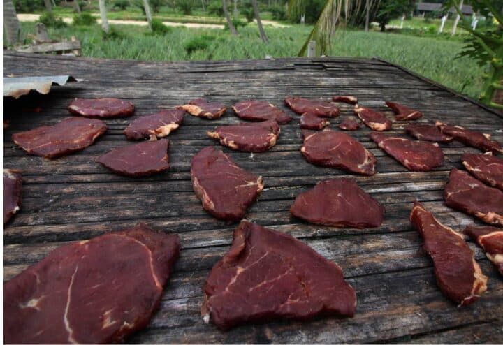 Some pieces of meat are sitting on top of a wooden table to dry for making pemmican from game meat.