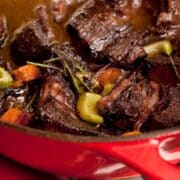 Beef stew in a red pot on a table.
