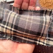 A small rectangular plaid sachet eco-friendly hand warmers filled with grains is held in a hand over a wooden surface. Scissors and scattered grains are visible in the background.