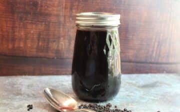 A jar of black pepper syrup next to a spoon.