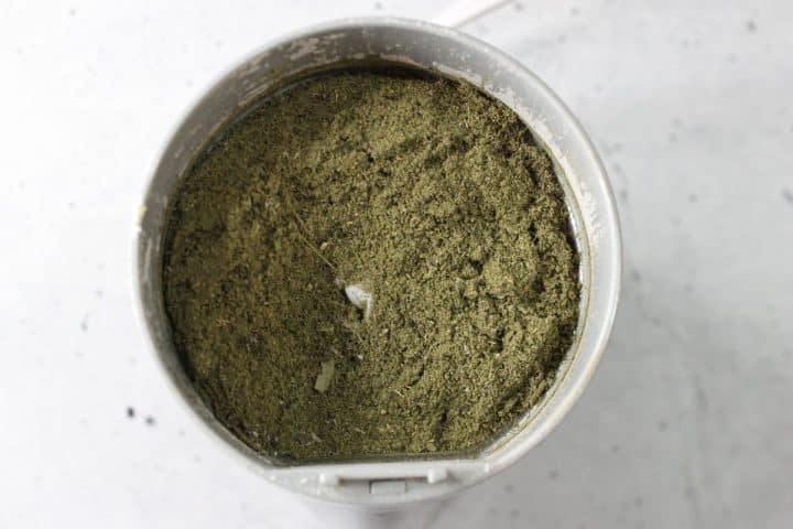 Top view of a grinder containing finely ground green herbal powder.