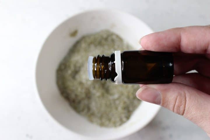 Hand holding a small brown bottle above a bowl of dry ingredients.
