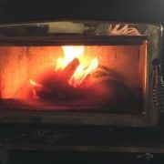 A lit wood-burning stove with visible flames and a glass door in a dimly lit room.