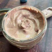 A jar of homemade calamine lotion open on a wooden table, with a spoon resting beside it.