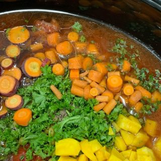 Chopped vegetables including carrots and yellow squash simmering in a slow cooker with herbs.