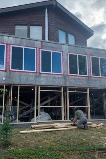 a homestead with a wrap around deck under construction and new windows being put in