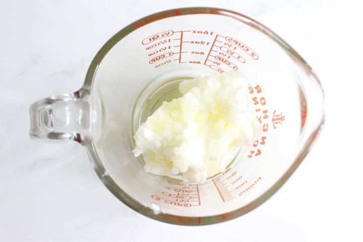 A glass measuring cup containing a white, rice-like substance, viewed from above on a white surface.