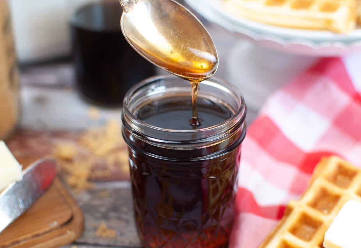 Spoon of homemade DIY pancake syrup over a mason jar on a wooden table.