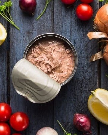 A picture of a can of fish surrounded by fresh vegetables
